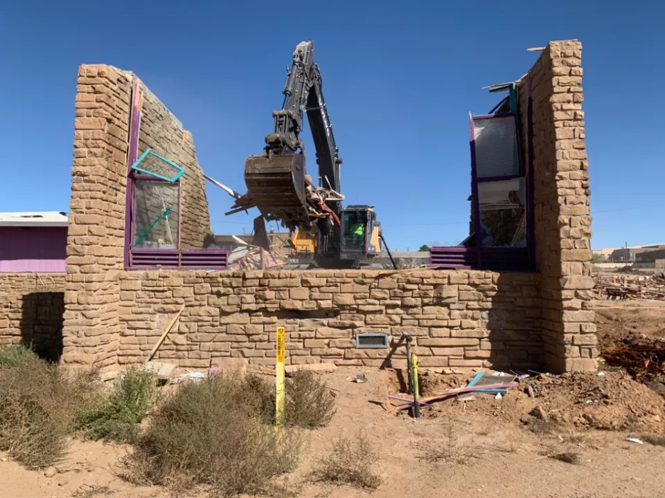 Demolition in progress of an excess building. A yellow excavator demolishes a stone building. 
