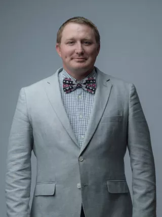 A man in a grey suit and bow tie poses for a headshot.