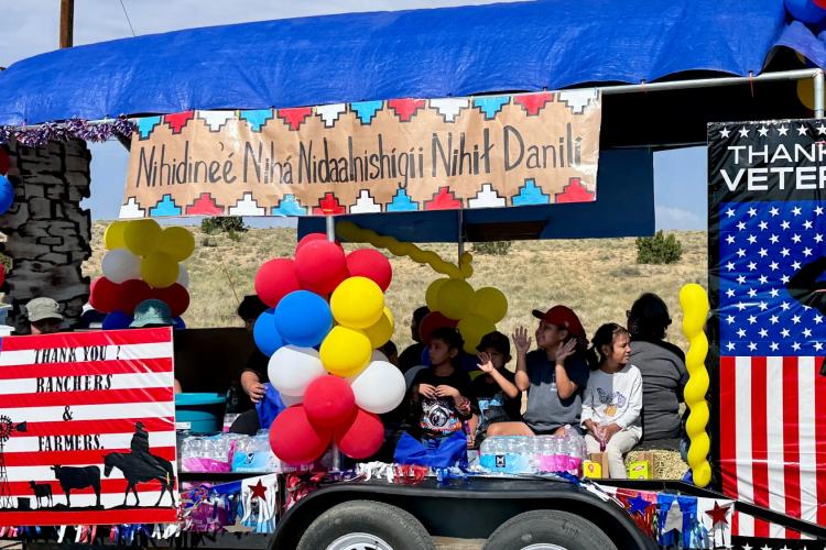 Students and community members ride on a trailer designed to be a parade float with posters and balloons.