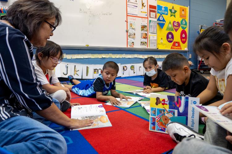 A teacher and her students read together as they sit on the floor in their classroom.