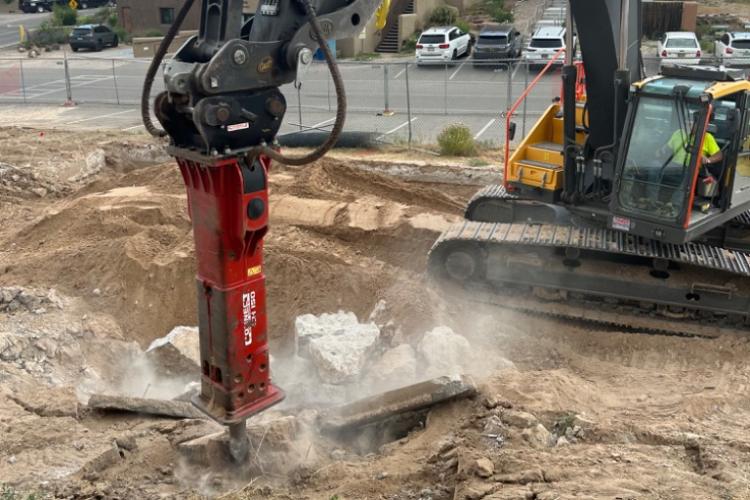 Excavator jackhammer clearing and breaking down dirt and stone at BIE school.