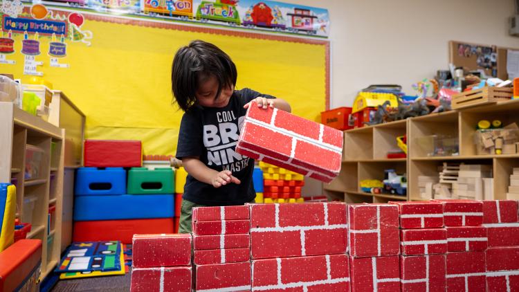 A young student builds a wall with toy bricks.