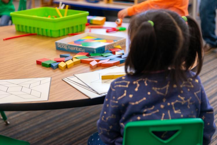 A student sits at a table facing away from the camera and looking at a project in front of them.