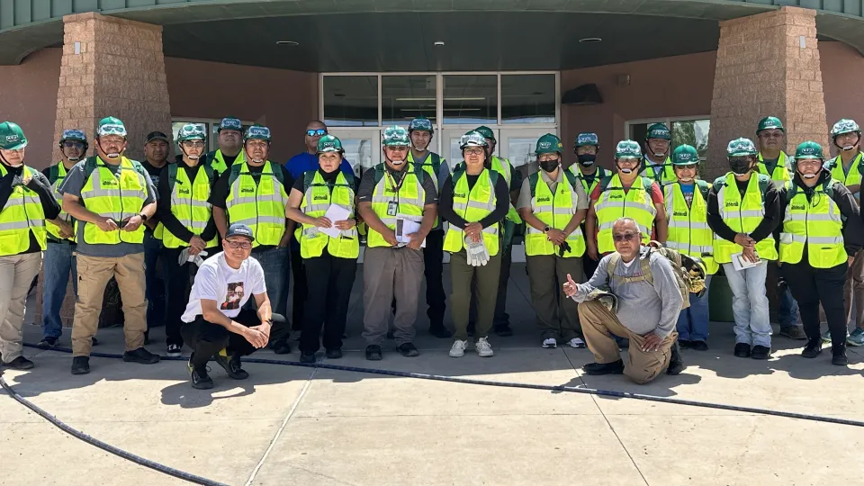 A group of people in safety gear stand and pose for a photo in front of a school building.