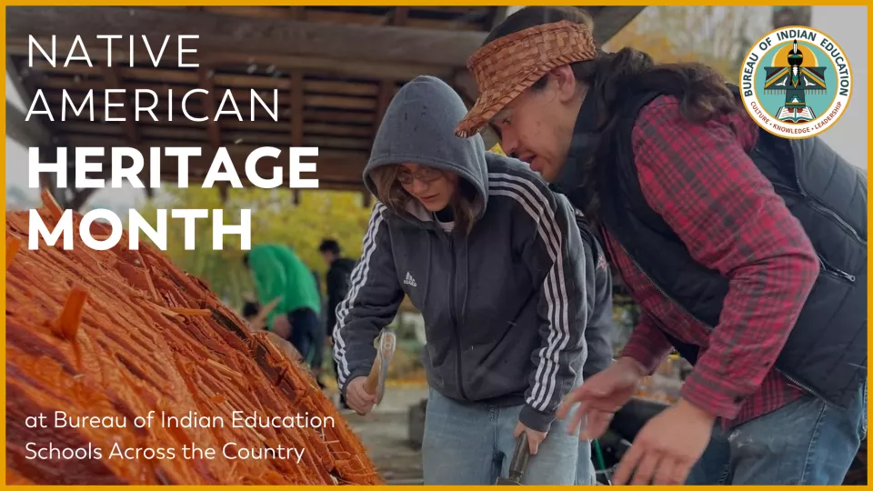 An adult and a student stand beside a huge piece of wood they are carving into a canoe.