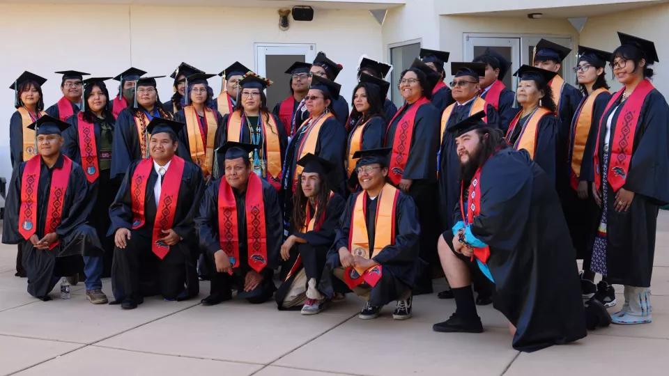 A group of graduates in black robes and red stoles poses for a photo.