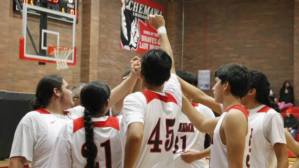 A group of basketball players in uniform raise their hand in a fist together before tip-off.