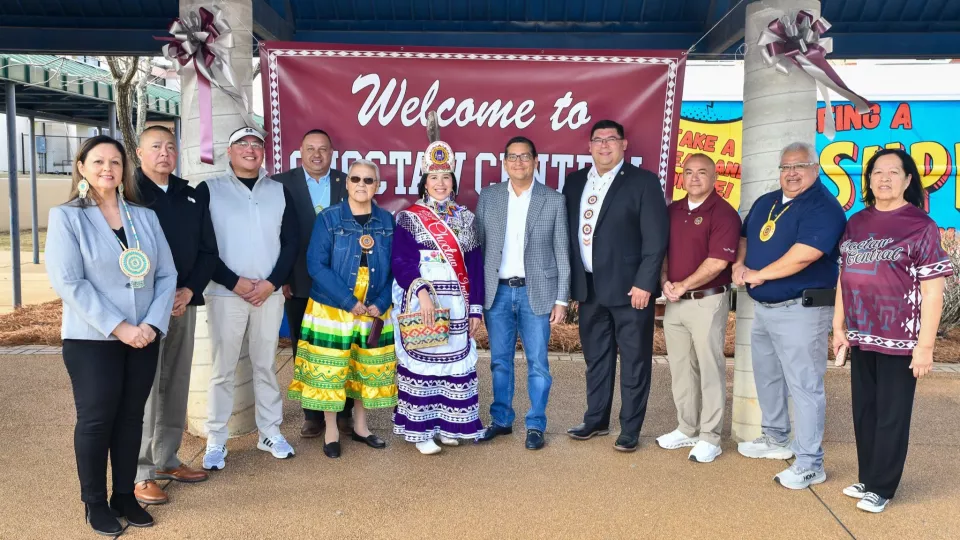 A group of people stand in a line outdoors in front of a banner for a photo.
