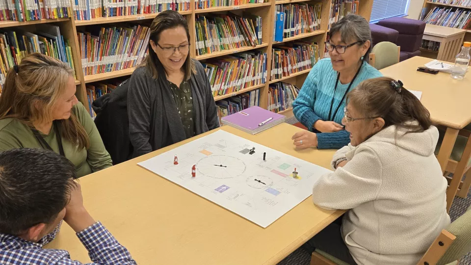 A group of people sit around a table in a library to play a board game.