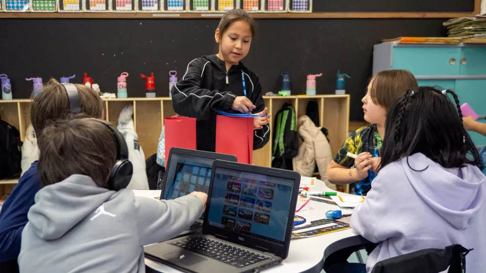 Five students sit around a table and listen to one of them give a presentation.