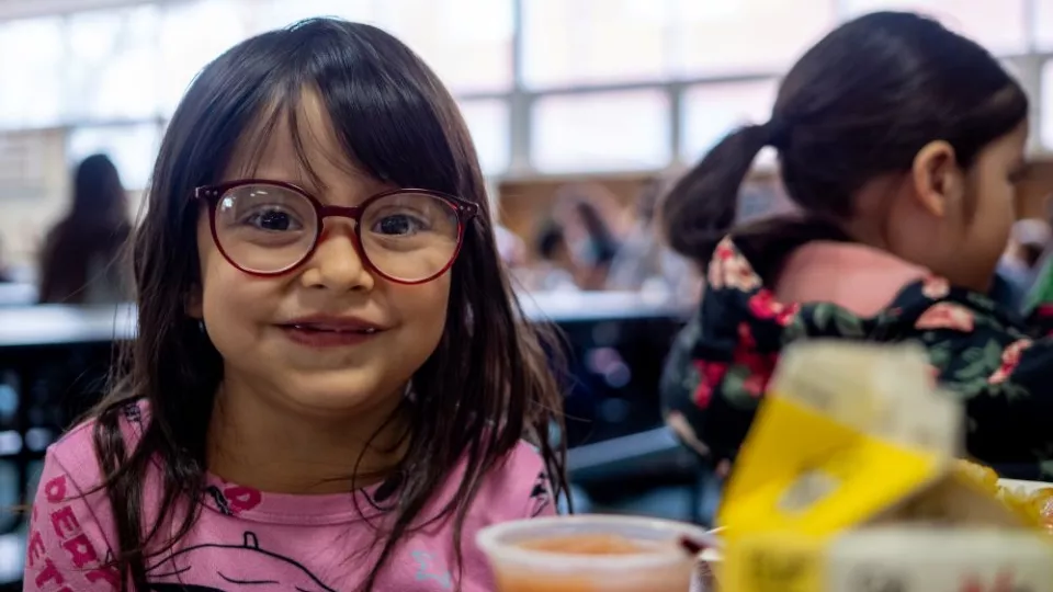 A young student sits a cafeteria table in front of a tray of food.