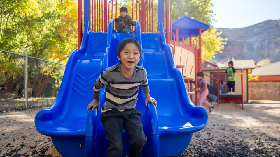 A child hops off the end of a large, blue slide after sliding down.