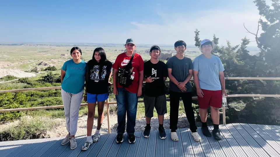A group of students pose for a group photo at a look out point in the mountains.