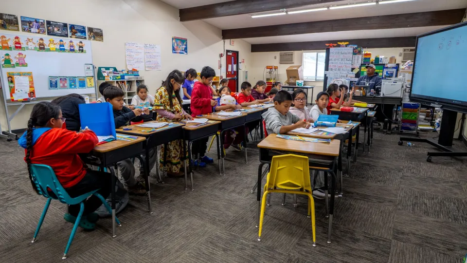 A classroom full of students sit at their desks and work on worksheets.