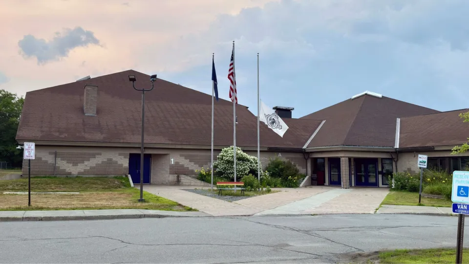 A brown school building with three flag poles in front of it.
