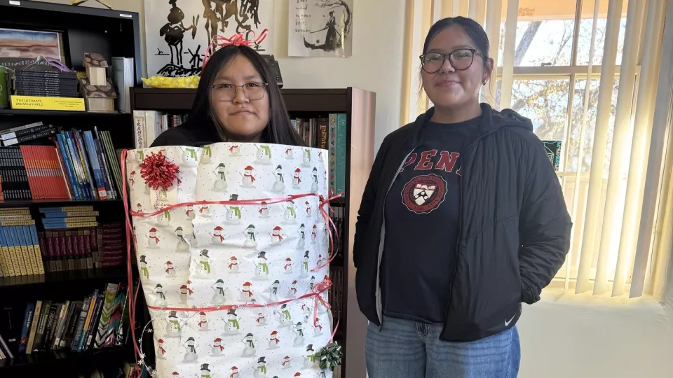 Two high schools students pose for a photo, one wrapped up in wrapping paper like a Christmas present.