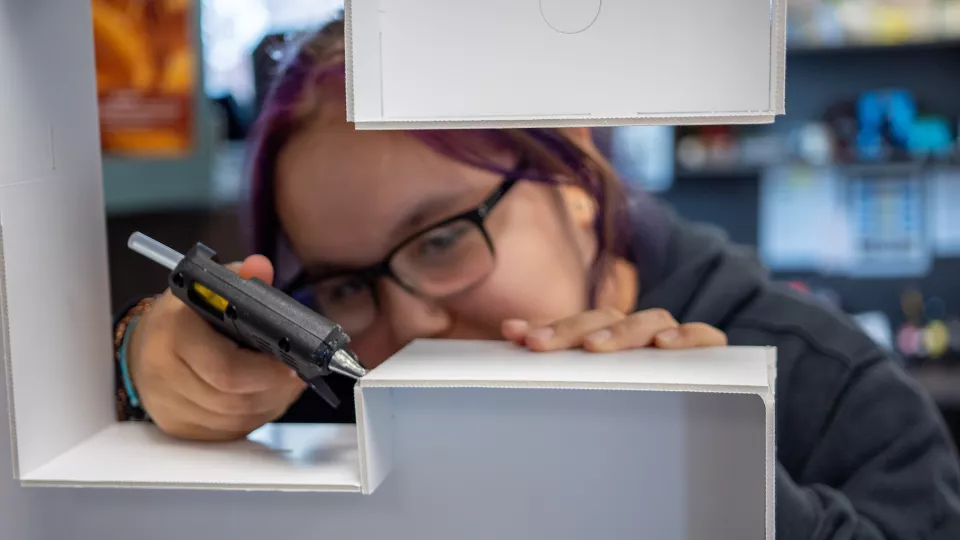 A student glues pieces of a display together with a hot glue gun.