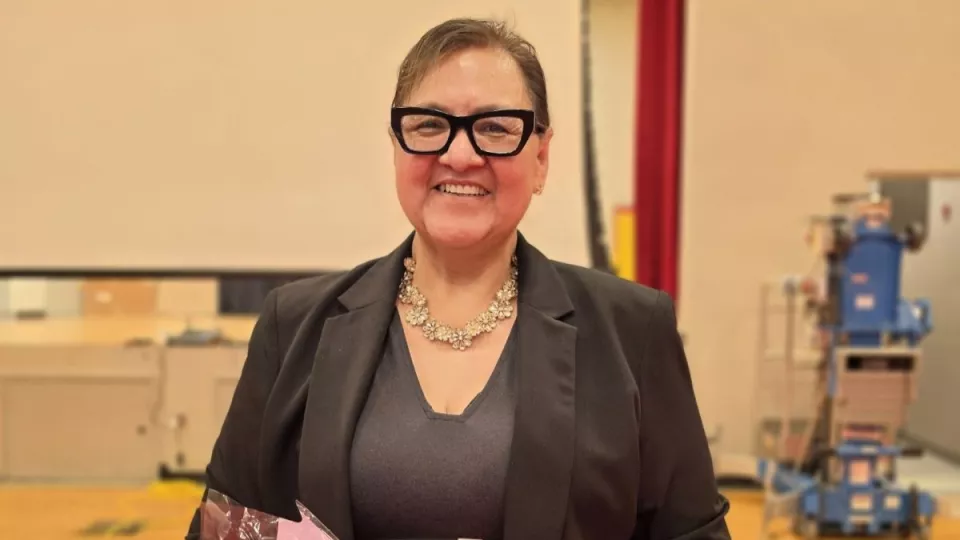 A woman in a blazer and black glasses holds a bouquet of flowers.