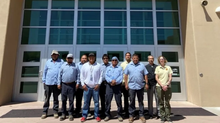 Ten adults stand and pose for a photo outside of a building with tall windows.