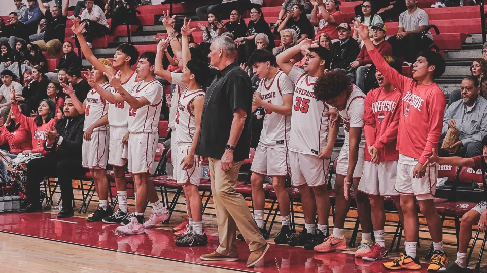 A basketball team in uniform cheer from the sidelines during a game.
