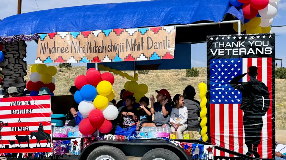 Students and community members ride on a trailer designed to be a parade float with posters and balloons.